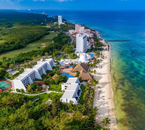 Vista de los edificios del hotel Melia Cozumel All Inclusive frente al mar junto a la playa y con la naturaleza y selva en la parte trasera.