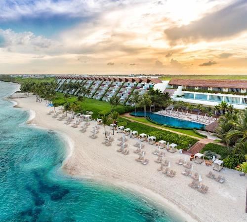 Foto del hotel Grand Velas Riviera Maya - All Inclusive donde se puede ver la enorme piscina junto a unos jardines cerca de la playa de color blanco donde hay unas camas para tomar el sol frente al mar