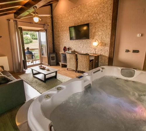 Foto del jacuzzi en el salón de la Casa Rural Aldekoa donde tienes una decoración de madera y estilo rústico con un ventanal al fondo con vistas al campo