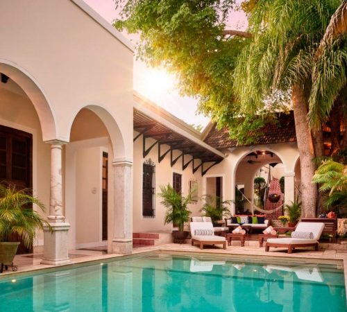 Foto de la piscina en el patio donde se ven unas hamacas y unas mesas bajo el arbol en Casa Lecanda Boutique Hotel