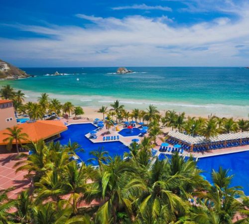 Vista de la playa al fondo con el mar de color turquesa y las palmeras junto al mar y la piscina en el Hotel Barceló Ixtapa - All Inclusive