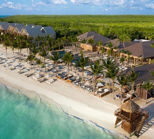 Vista de la playa con arena blanca y aguas de color turquesa del hotel Banyan Tree Mayakoba en Playa del Carmen rodeado de naturaleza y con camas balinesas frente al mar.