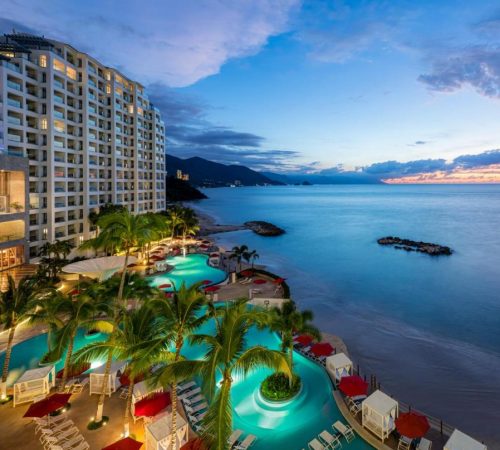 Vista desde el aire donde se puede ver el hotel Hilton Vallarta Riviera All-Inclusive Resort y sus piscina frente al mar en el atardecer.