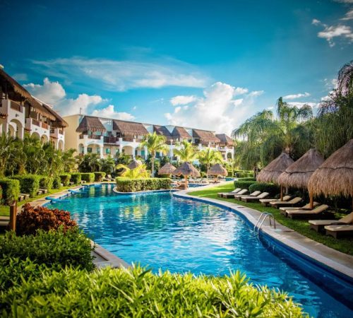 Vista de las piscinas rodeadas de los alojamientos con casas individuales frente a las tumbonas para tomar el sol en Valentin Imperial Riviera Maya All Inclusive