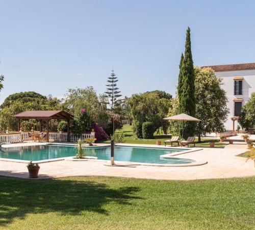 Vista de los jardines, los árboles, la piscina y la casa señorial al fondo en el hotel Hacienda las tres niñas