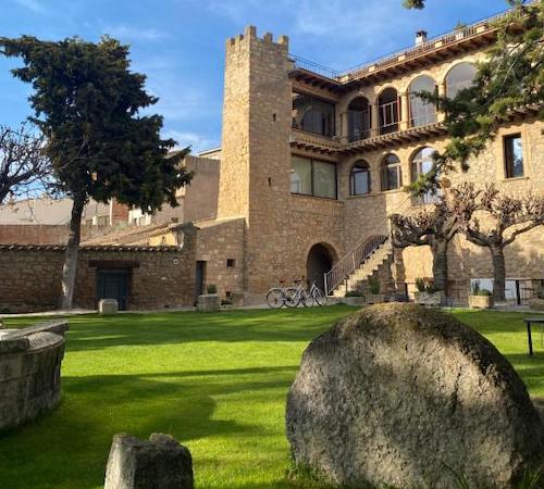 Foto desde el jardín con cesped y árboles en Casa Llobera 1792 donde se ve el hotel construido en piedra al fondo.