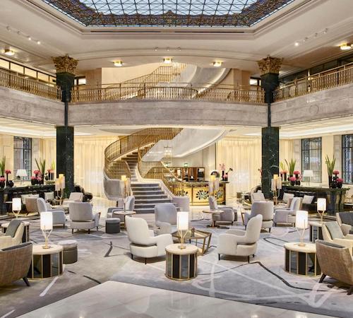 Foto del impresionante hall del hotel Four Seasons Hotel Madrid con mobiliario de estilo elegante, suelos de mármol, una escalera de mármol al fondo y una techo con vidriera.