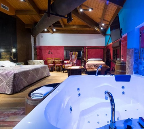 Foto del jacuzzi frente a la cama en la suite decorada con madera y piedra del hotel SPA El Lagar de Isilla