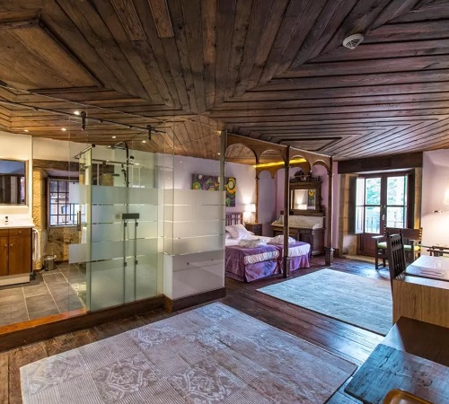 Habitación con techos de madera y decoración rústica con el baño acristalado frente a la cama en la suite elegante de Pazo da Pena Manzaneda