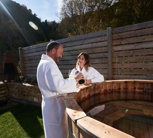 Pareja disfrutando de una botella de cava junto a la bañera de hidromasaje al aire libre de madera en Caserío Montehermoso
