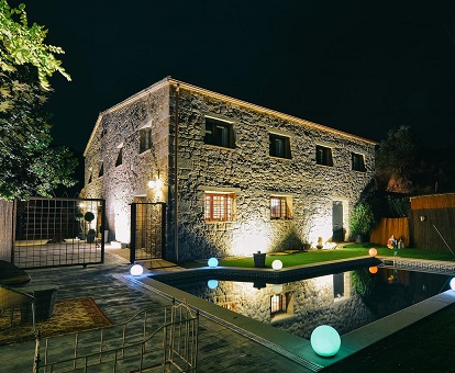 Foto del exterior por la noche y junto a la piscina donde se puede ver lo bonita y rústica que es esta masia en Vila caelus que se ha convertido en un hotel para adultos con mucho encanto.